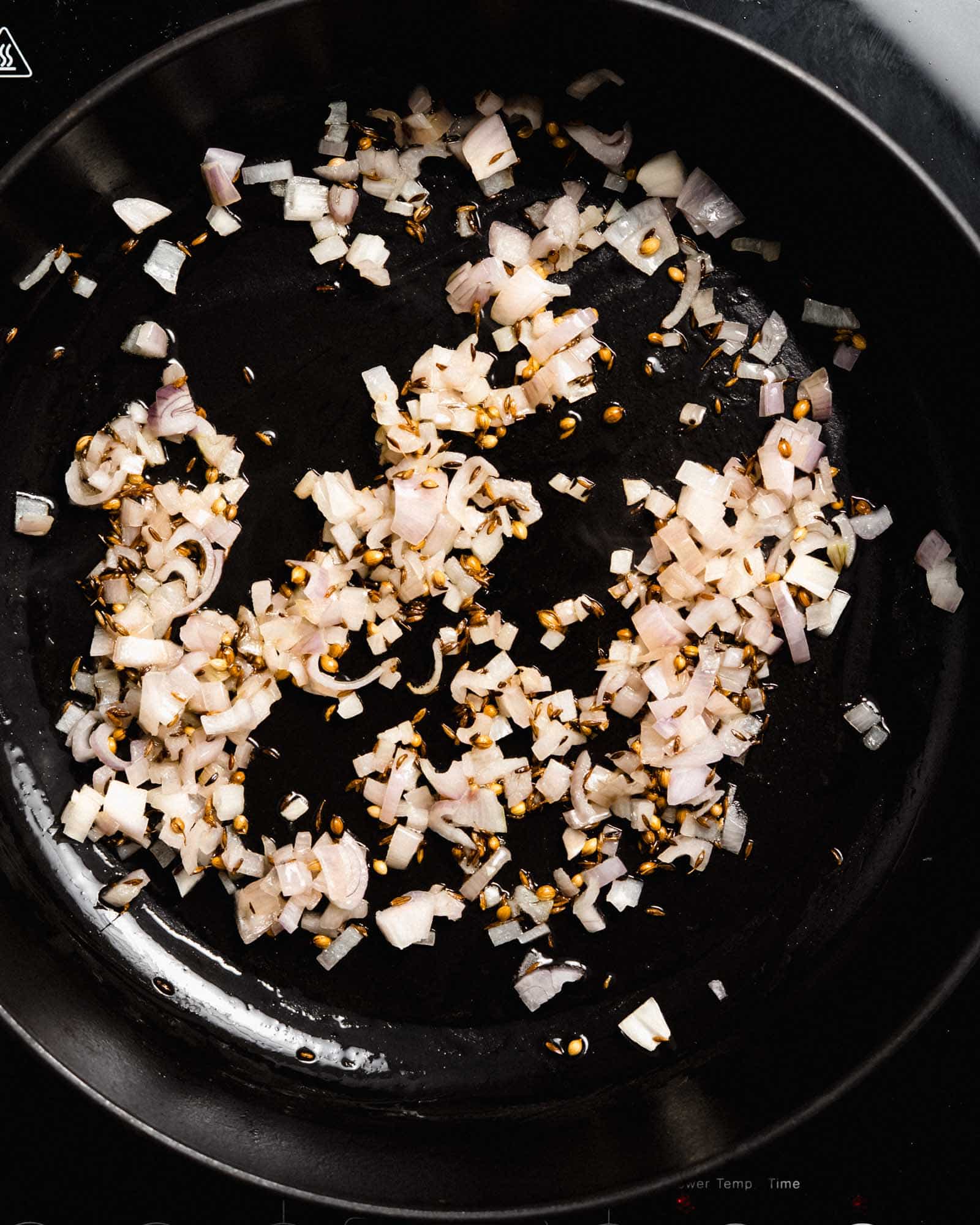 Fried cumin seeds, coriander seeds and onion in a pan.