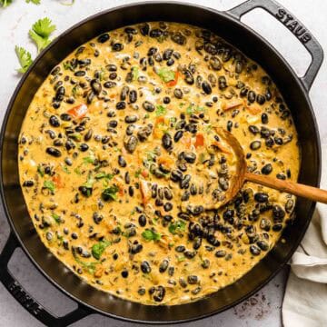 Birds eye view of a bean curry in a large saucepan with a wooden spoon in it.