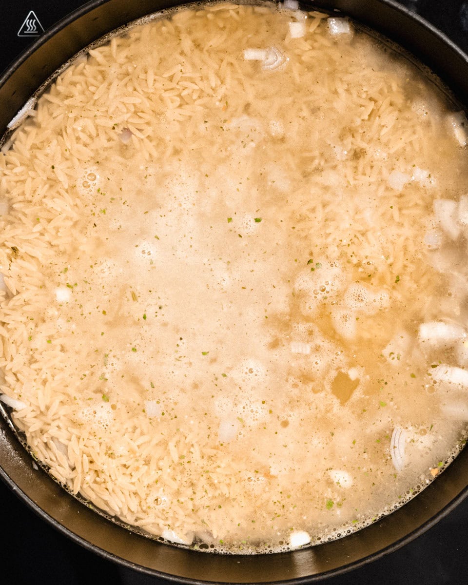 Orzo and veggie broth added to onion and garlic in a pan.