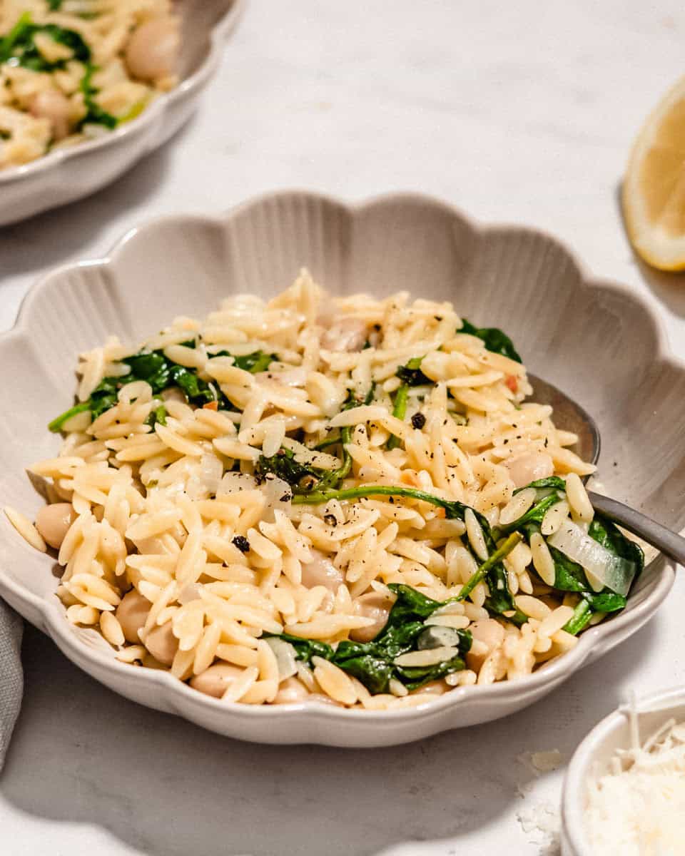 Lemon spinach orzo in a bowl next to it some fresh parmesan and a lemon.