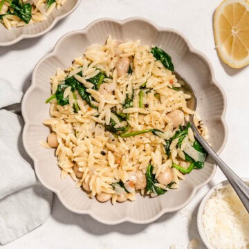 Birds eye view of lemon spinach orzo in a bowl next to it some fresh parmesan and a lemon.