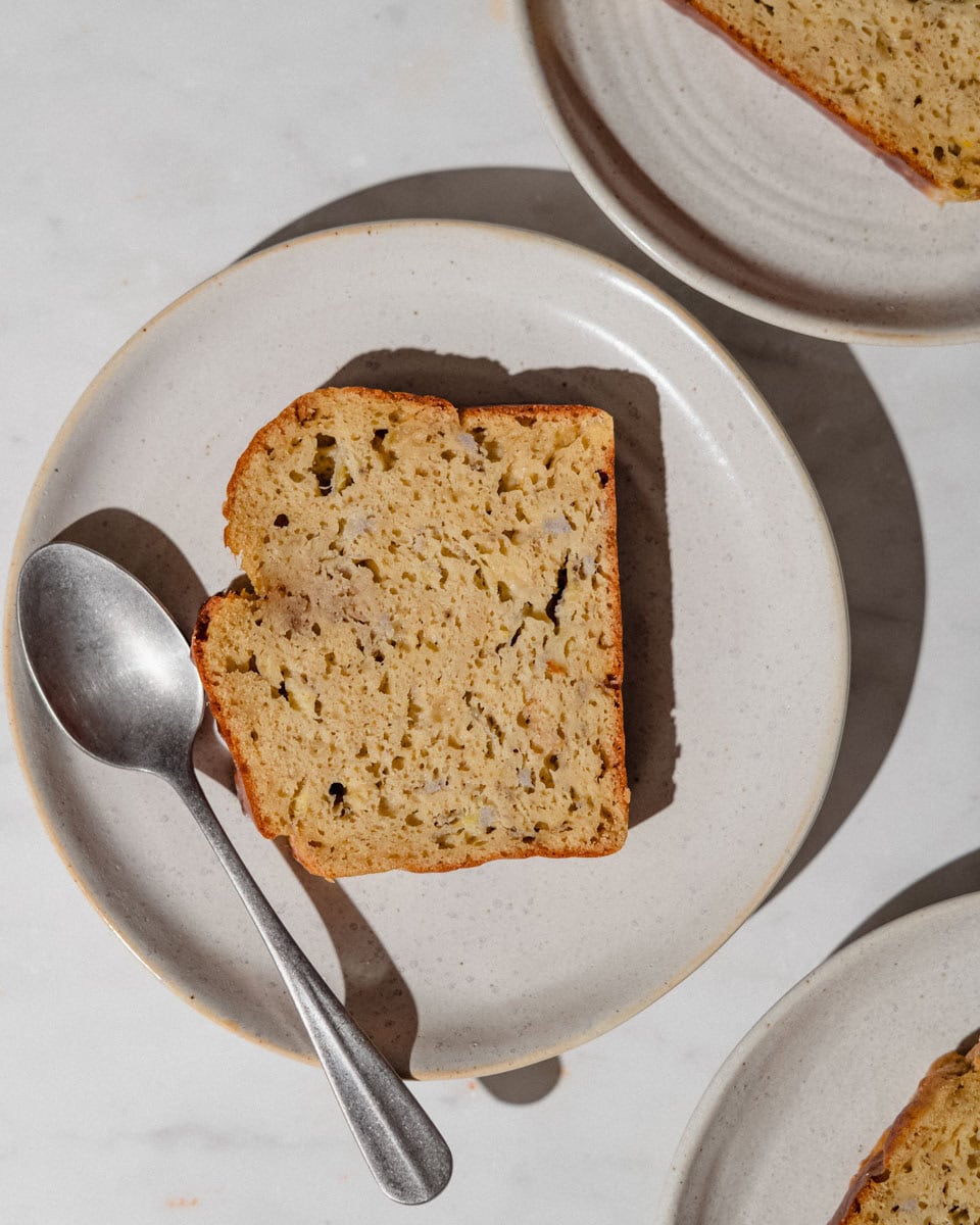 A slice of peanut butter banana bread on a speckled ceramic plate with a vintage spoon, shown from above.