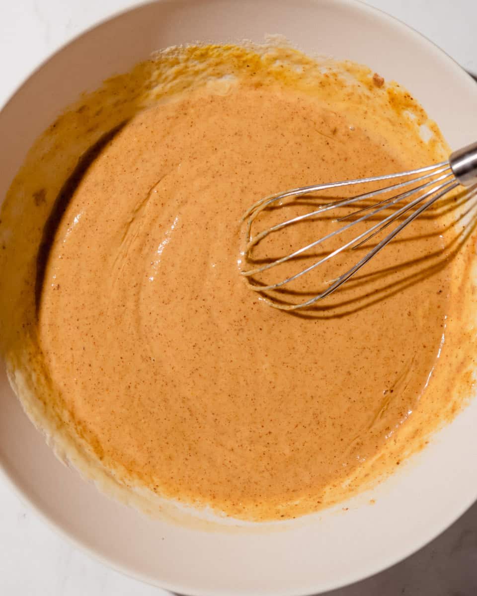 Wet ingredients whisked together into a smooth orange batter in a large bowl.