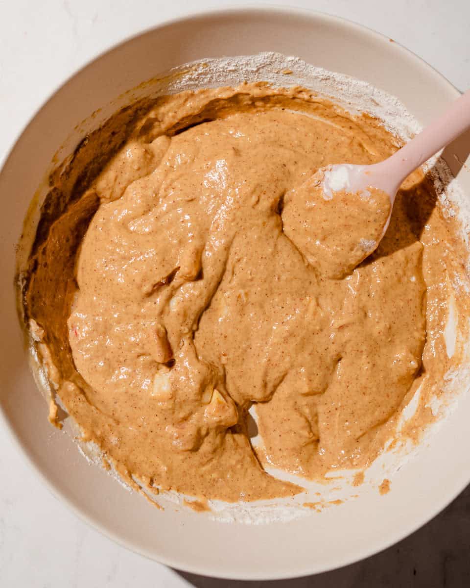 Thick pumpkin apple batter folded together with a pink spatula in a large bowl