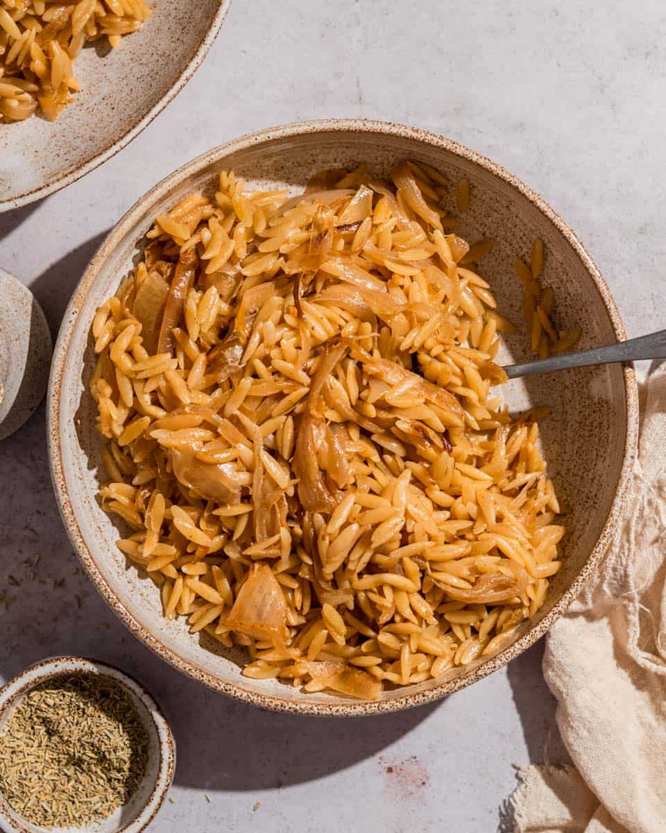 French onion orzo on a serving plate next to it some dried rosemary.