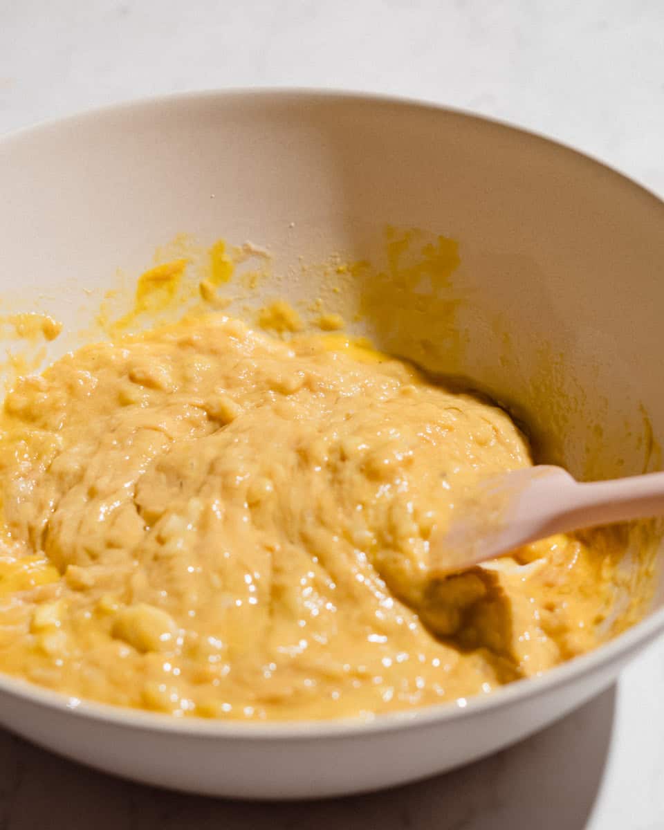 Mashed bananas, peanut butter and eggs stirred together into a wet batter with a pink spatula.