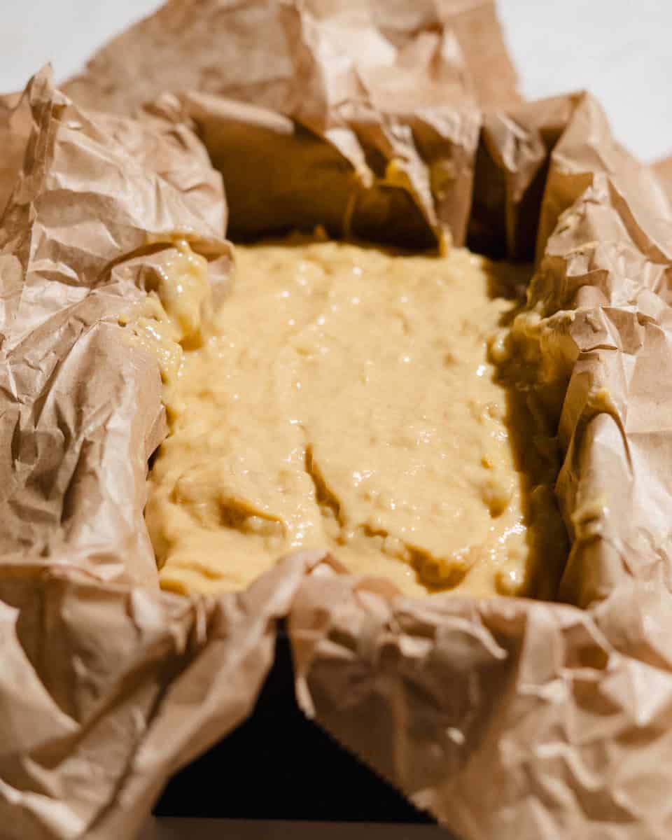 Banana bread batter spread in a loaf pan lined with parchment paper, ready to bake.