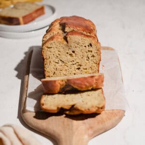 A loaf of peanut butter banana bread on a wooden serving board, with two slices cut to show the soft, moist crumb.